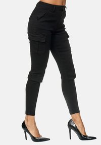 Schwarze Cargo-Hosen aus Denim mit taillierter Passform, mehreren Taschen und umgeschlagenen Säumen, kombiniert mit schwarzen High-Heels.
