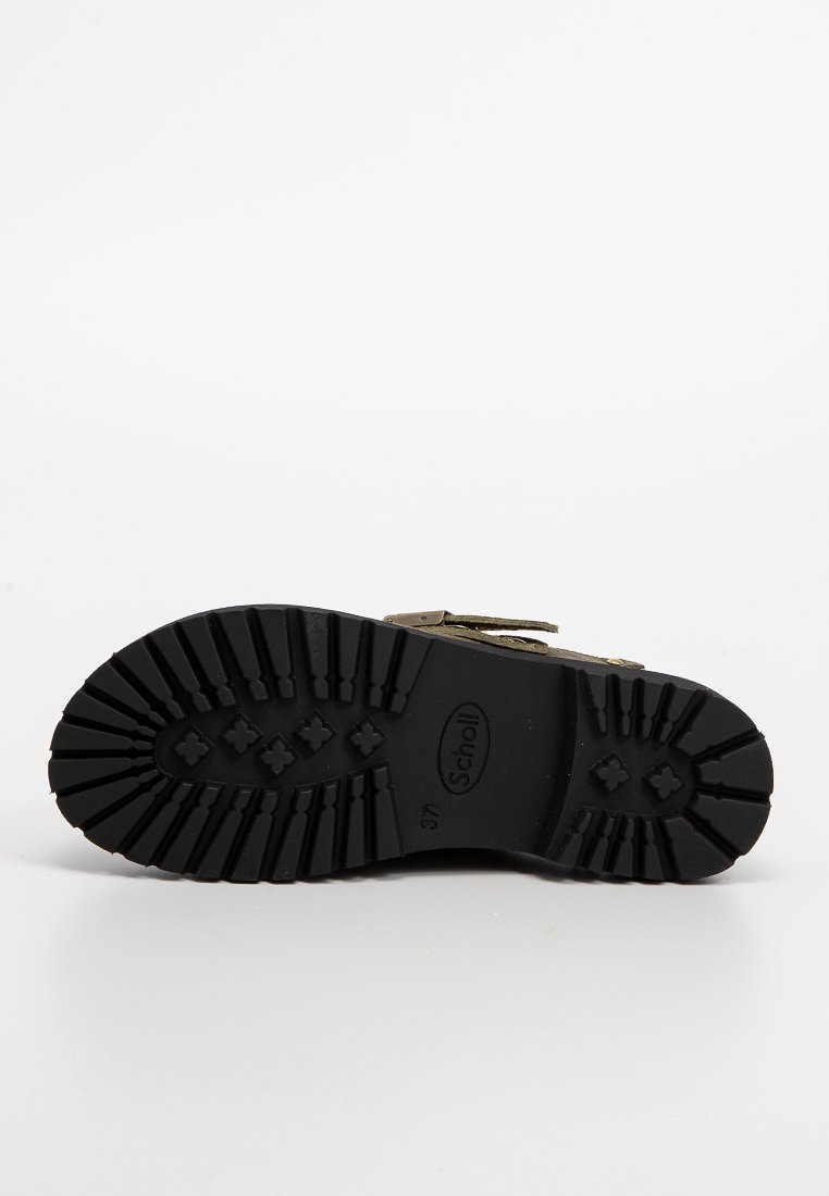 Suola di una scarpa nera di misura 37 con profonde scanalature, modelli a forma di croce e il nome del marchio "Scholl" impresso al centro.