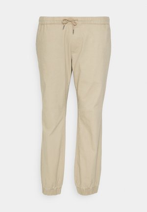 Pantaloni bej deschis, tapered, din material moale, cu o talie elastică și șnur, și manșete elastice la glezne.