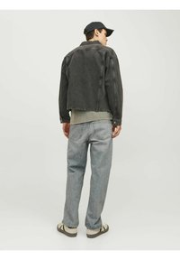 Chaqueta de mezclilla gris oscuro sobre una camisa gris claro, combinada con pantalones vaqueros azul claro y sandalias beige. Diseño sencillo con hardware mínimo.