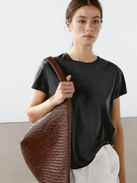 Sort kortærmet t-shirt parret med en vævet brun håndtaske. Tasken har en struktureret overflade og en bred, flad rem.