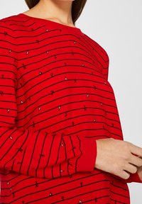 Rood t-shirt met lange mouwen, horizontale zwarte strepen en kleine hart- en strikafdrukken. Zachte stof met een ronde halslijn en gathered manchetten.