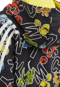 Sudadera con capucha de tela negra con estampados de personajes de dibujos animados coloridos. Presenta franjas blancas y una capucha forrada en amarillo.