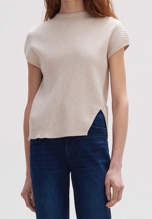 Beige geribbelde korte mouw trui met diagonaal patroon en zijsplit, gedragen met donkerblauwe spijkerbroek door een staand persoon.