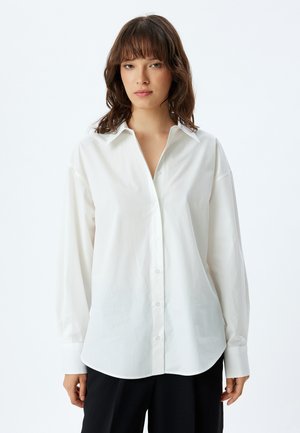 Camisa blancas de botones con un cuello clásico, mangas largas y un corte recto. Fabricada en un tejido suave con un ligero brillo.