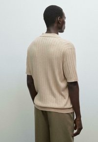 Beige kortærmet polo skjorte med vertikal ribbede tekstur, der har en blød krave og en afslappet pasform. Båret med lyse, brede bukser.