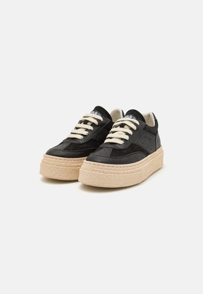 Svarta sneakers med en upphöjd strukturerad sula i ljusbeige, med vita snören och subtila perforerade detaljer på sidorna.