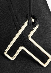 Borsa a tracolla nera in pelle con un accento geometrico dorato. La texture è liscia con cuciture visibili lungo i bordi.