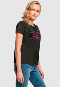 Black short-sleeve t-shirt featuring a bold AC/DC logo in red and silver, made of cotton with a relaxed fit and crew neckline.