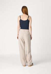 Marineblauw tank top met smalle bandjes, gecombineerd met beige wijde broekspijpen met achterzakken en een elastische tailleband. Dure textuur.
