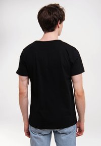 Camiseta de algodón negra con cuello redondo, mangas cortas y corte relajado, combinada con jeans de mezclilla azul claro. Sencilla, sin gráficos visibles.