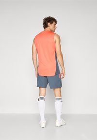 Sportstøj med en ærmeløs koralfarvet skjorte og grå shorts. Fremhævet med sorte striber på hvide sokker og hvidt fodtøj.