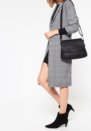 Grau karierten lange Mantel mit einer taillierten Silhouette, schwarze Lederhandtasche mit geprägtem Design und schwarze Wildleder-Stiefeletten mit spitzem Zeh.