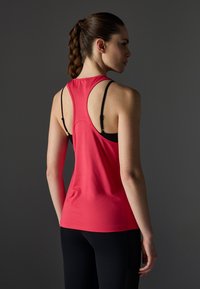 Magenta sportlik tank top, millel on jooksja seljaosa disain ja mustad rihmad, valmistatud siledast kangast. Paigutatud tumeda tausta vastu.