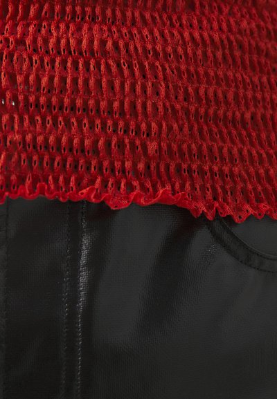 Rød, teksturert mesh topp med volangkant i kombinasjon med glatt svart stoff, som viser et enkelt og stilrent design med buet halslinning.