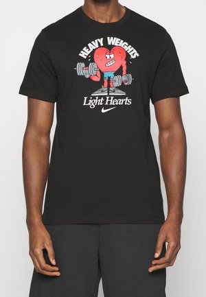 Camiseta de algodón negra con un dibujo de un corazón de dibujos animados levantando pesas. Texto gráfico "PESAS PESADAS" arriba, "Corazones Ligeros" abajo, con el logo de Nike.