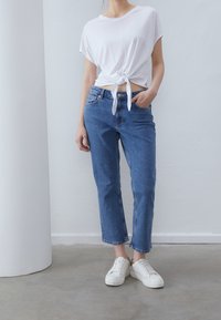 Vit knuten t-shirt, högmidjade blå jeans och vita sneakers. Avslappnad outfit med en ledig passform och minimalistisk design.