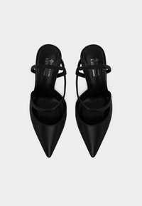 Μαύρα γόβες με μυτερή μύτη, πίσω λουράκι και λεπτές λωρίδες, με επενδυμένα πέλματα που φέρουν την ετικέτα "bedford vegan".