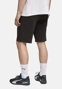 Sorte bomuldsbukser med lige snit, med et rødt logo. Sat sammen med hvide ankelstrømper og sorte sneakers med grå detaljer.