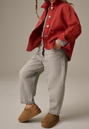 Czerwona kurtka dżinsowa, pasiasta koszula, jasnoszare luźne dżinsy oraz brązowe zamszowe buty wsuwane. Strój charakteryzuje się kontrastującymi kolorami i teksturami.