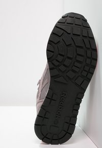 Graue Sportschuh mit einer strukturierten Mesh-Oberfläche und Gummisohle, die ein Profilmuster aufweist. Der Markenname "Reebok" ist auf der Sohle sichtbar.