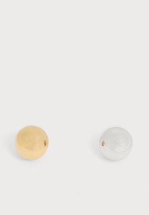 Deux boules métalliques lisses et rondes placées côte à côte sur un fond blanc, une dorée et une argentée.