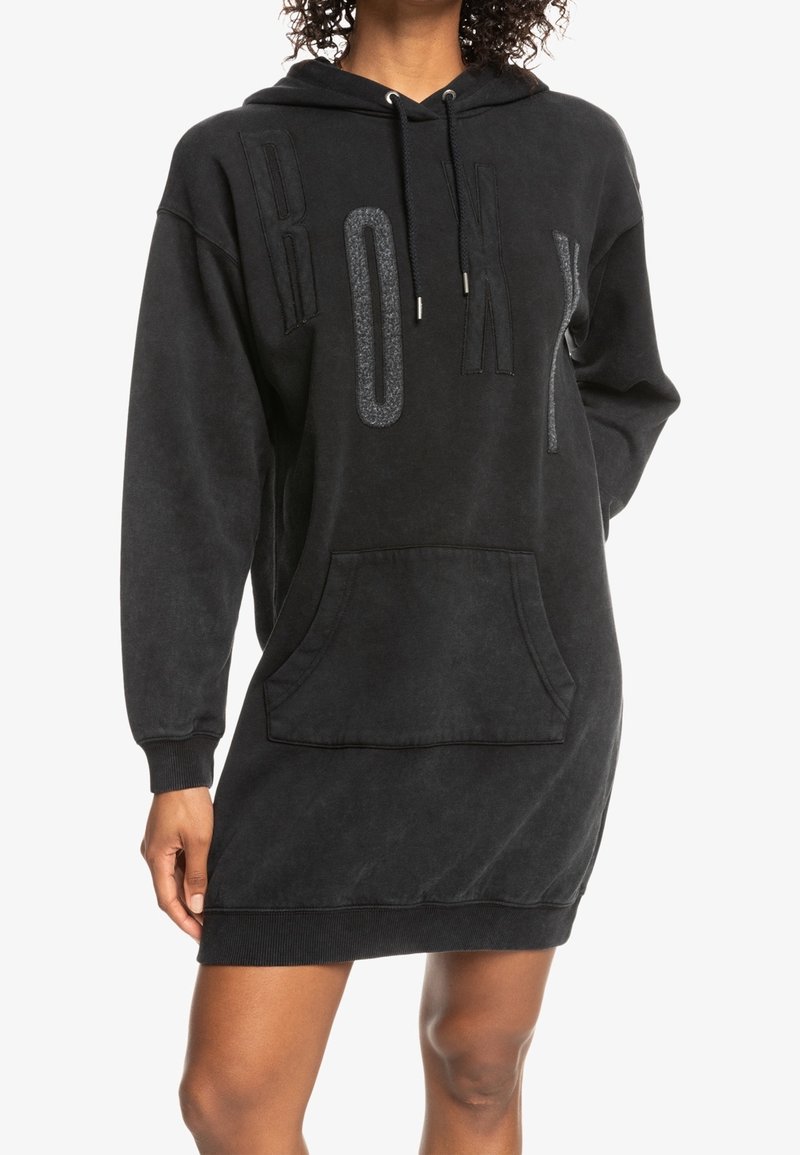 Robe hoodie noire en tissu doux, avec une poche avant, des poignets côtelés et un lettrage 'ROXY' audacieux dans un motif texturé.