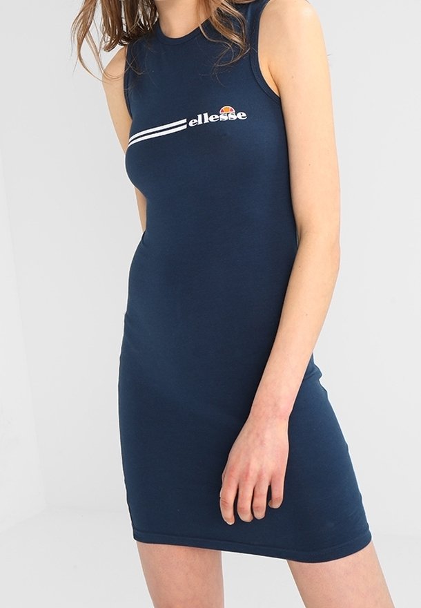 Femme portant une robe bleu marine ajustée sans manches avec le logo "ellesse" et des rayures blanches sur la poitrine.