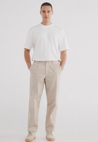 Chinos beige con vestibilità dritta, abbinati a una t-shirt bianca a maniche corte. Le scarpe sono di un beige chiaro con un design minimale.