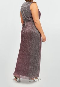 Sukienka maxi w odcieniach fioletu z metalicznymi fałdami, bez rękawów, z regulowanym wiązaniem w talii, połączona z srebrnymi obcasami.