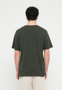 T-shirt in cotone verde oliva con maniche corte, scollo rotondo e vestibilità rilassata. Texture liscia, design minimalista e senza motivi visibili.