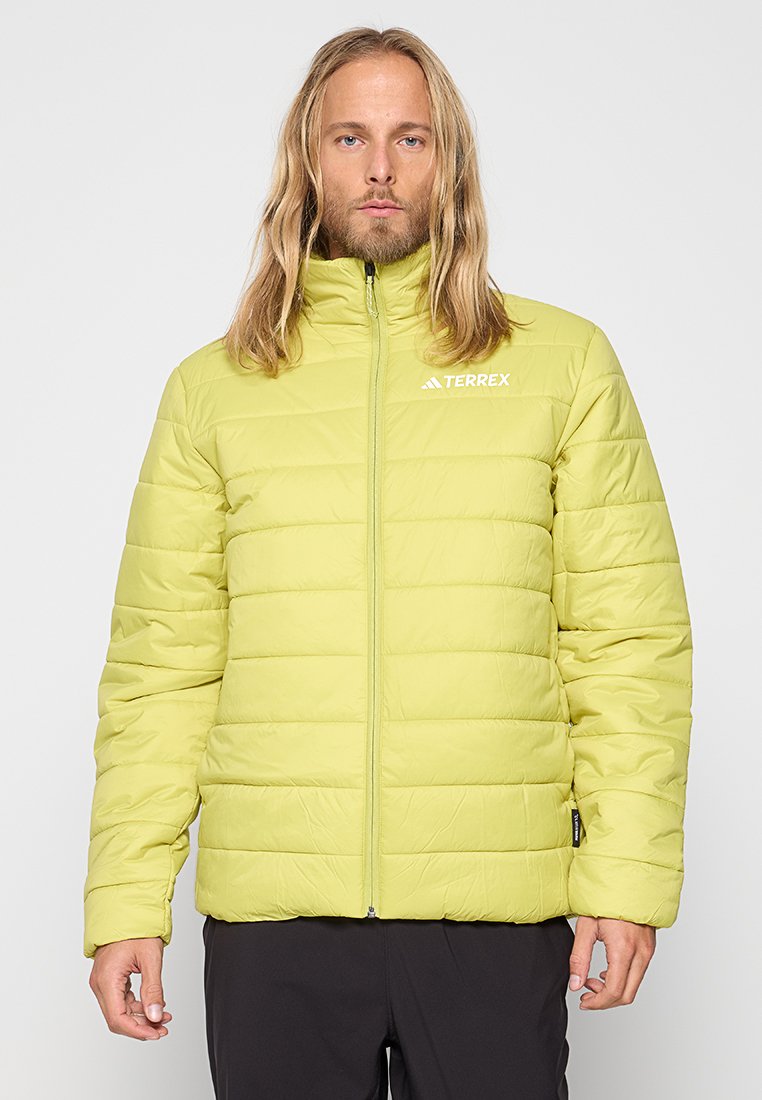 Chaqueta aislante de color verde claro con diseño acolchado, cuello alto, cierre de cremallera y logo en el pecho izquierdo; textura suave y silueta moderna.