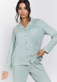 Conjunto de pijama verde con canalé, de manga larga, con cierre de botones en la parte delantera y bolsillo en el pecho. Presenta ribetes blancos en el cuello y los puños.