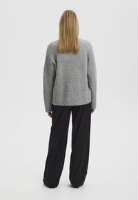 Grijze gebreide trui met lange mouwen, relaxte pasvorm, gecombineerd met zwarte wijde broek, gezien vanaf de achterkant.