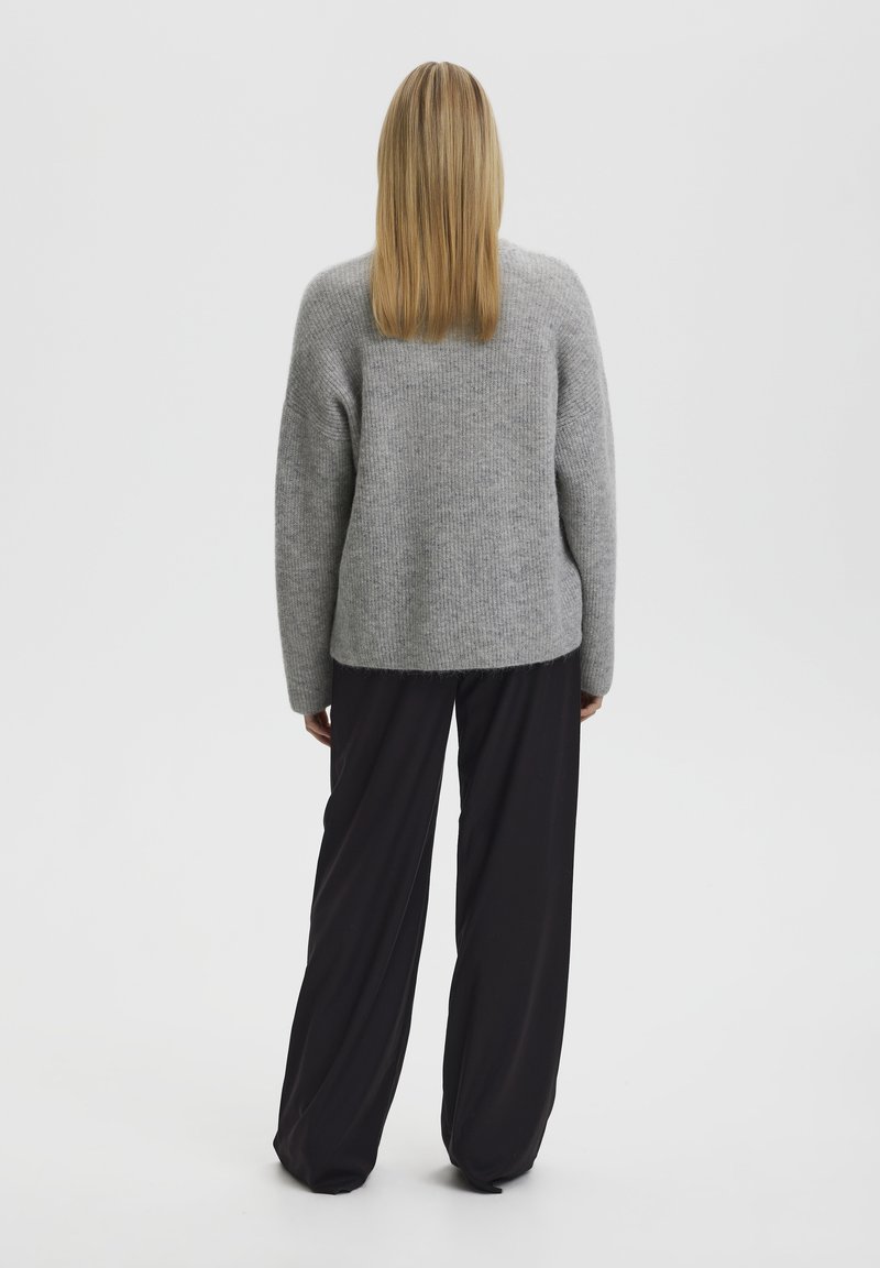 Grauer Strickpullover mit langen Ärmeln, lockerer Passform, kombiniert mit schwarzen weit geschnittenen Hosen, von hinten gesehen.