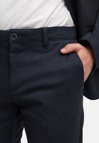 Pantaloni a spina di pesce blu navy con frontale liscio, tasche laterali e chiusura con bottone, caratterizzati da una texture morbida e una vestibilità su misura.