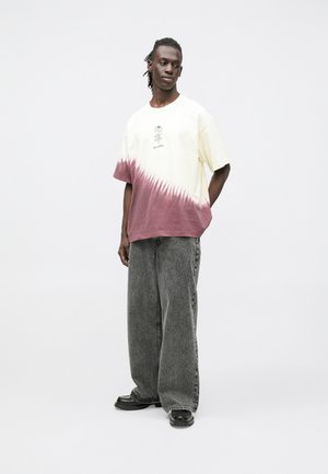 Īsām piedurknēm ar gaiši dzeltenu t-kreklu, apakšā ar rozā dip-dye dizainu un ziedu grafiku priekšpusē, kopā ar platām pelēkām džinsa biksēm.