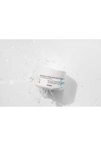 Pot blanc étiqueté "Crème Enrichie en Pouvoir Hydratant" avec des accents bleus, entouré d'eau éclaboussante, présentant une texture mate lisse.
