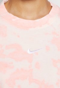 Sudadera de tie-dye rosa claro con cuello acanalado, que presenta un pequeño logo blanco de Nike centrado en el pecho. Material de algodón suave.
