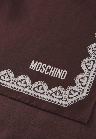 Brauner Stoff mit weißer Spitzenbordüre und "MOSCHINO" in Weiß nahe dem Rand bedruckt.