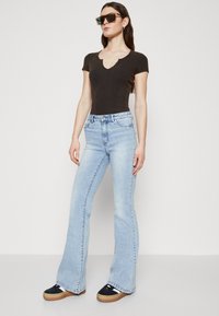 Svart ribbet kortermet bodysuit, lyseblå flared jeans og platåsneakers med svarte og beige detaljer. Klare solbriller fullfører stilen.