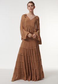 Robe brune en couches, fabriquée dans un matériau léger, avec un décolleté en V, des manches longues, et un buste à volants avec des sections de jupe en plusieurs étages.