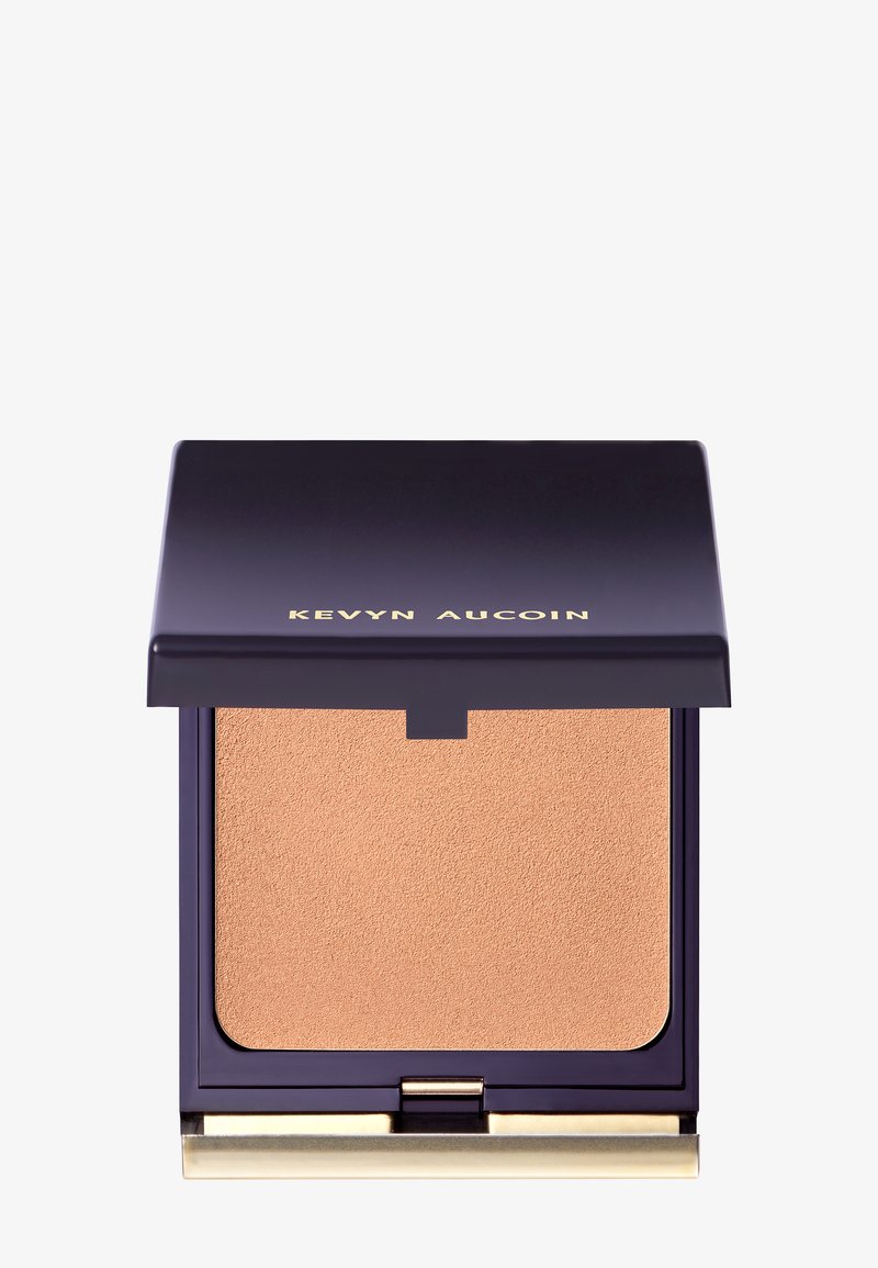 Compact powder with a purple case and gold accents. Textured surface of powder is light brown. Clamshell closure.