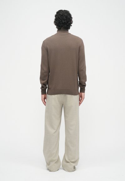 Pull en maille ajusté marron avec un col haut et des poignets côtelés, associé à un pantalon beige clair, ample, comportant un motif texturé.