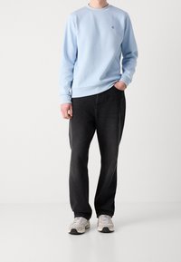 Sweatshirt bleu clair avec des poignets et un col côtelés, associé à un pantalon noir et des baskets beiges. Design simple et décontracté sans motifs.