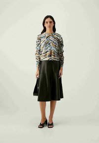 Farbiger Langarm-Pullover mit abstraktem Muster, kombiniert mit einem schwarzen A-Linien-Ledrock. Das Modell steht mit einer schwarzen Tasche und blockabsatzschuhen.