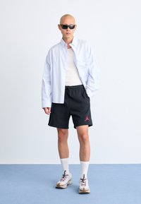 Hvid skjorte med blå striber, hvid top, sorte shorts med rødt logo, hvide sokker og sneakers i neutrale farver.