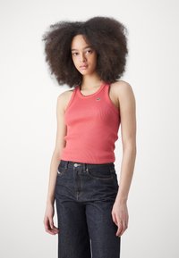 Rosa ribbad linne med rund halsringning, prytt med en liten grön logotyp. Matchas med högmidjade mörkdenimjeans.