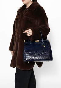 Borsa blu con stampa a forma di coccodrillo, dalla forma strutturata, con dettagli in oro e manico superiore, indossata con un cappotto in pelliccia sintetica marrone.