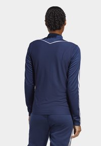 Marineblaues langärmeliges Sportshirt mit einem strukturierten Muster, weißen Akzentstreifen an den Ärmeln und einem erhöhten Kragen, der den Rücken betont.
